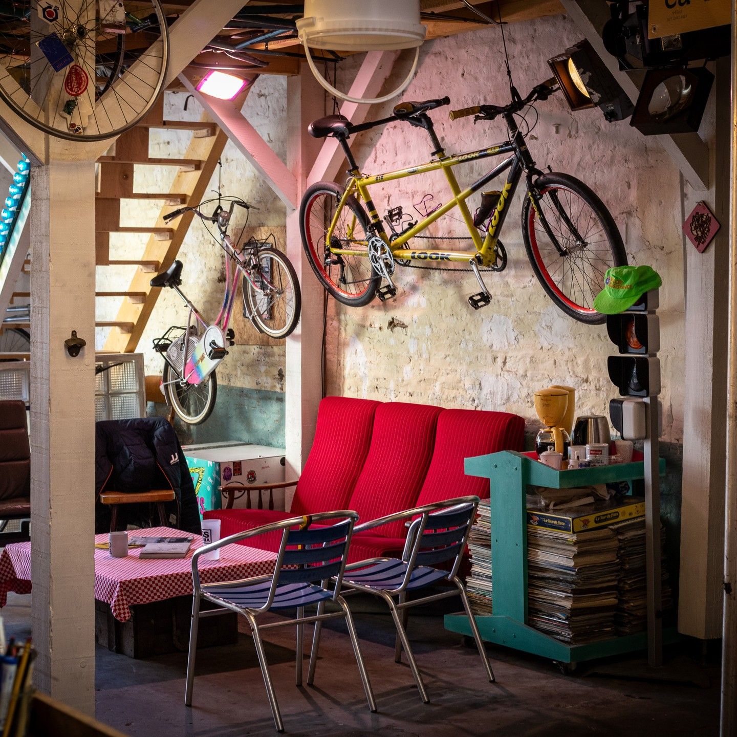 Le coin salon de l'atelier : canapé rouge, tandem jaune accroché au mur et vélos anciens
