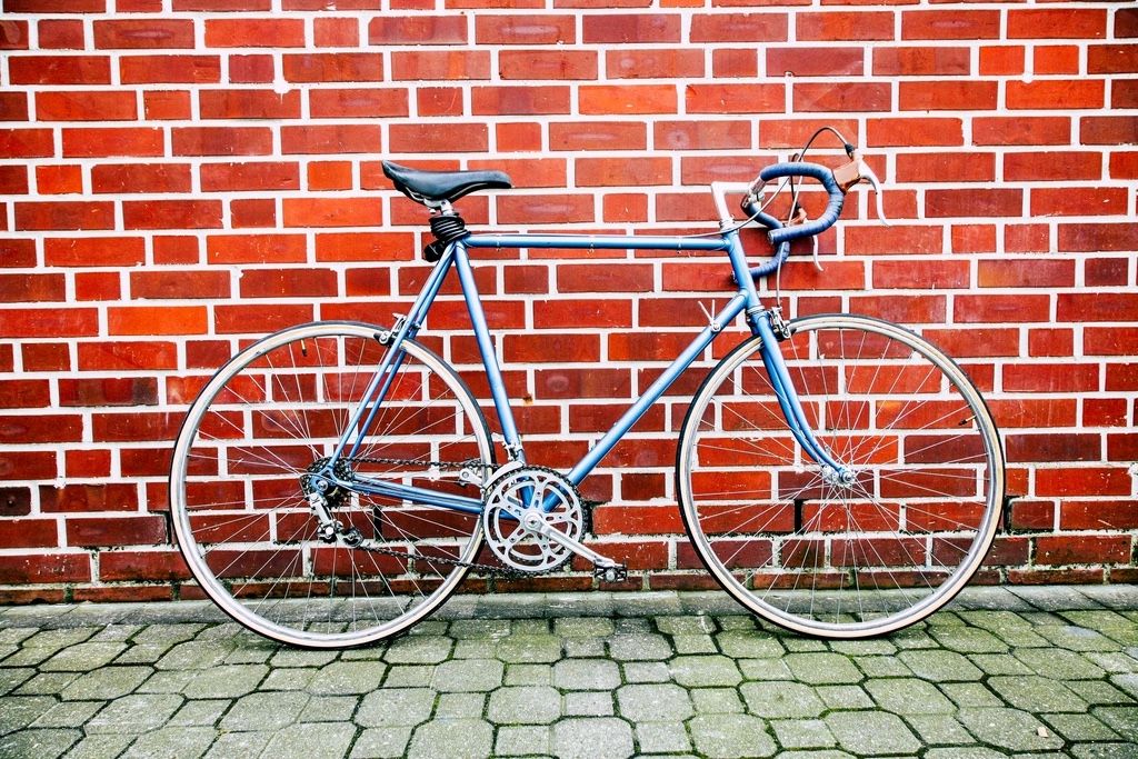Vélo de route vintage bleu à cadre acier, appuyé contre un mur de briques