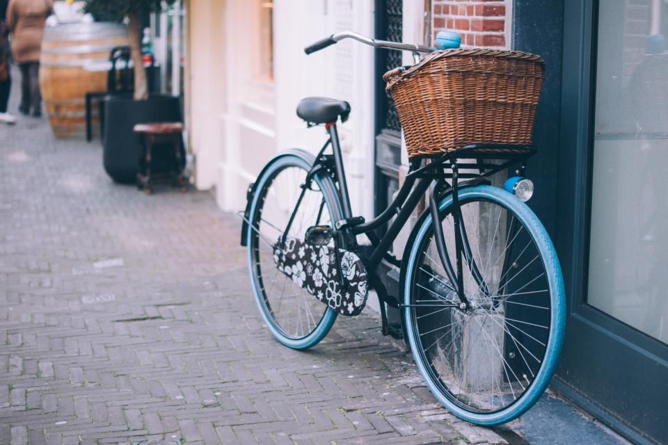 Vélo de ville bleu canard avec panier en osier, garé devant une vitrine